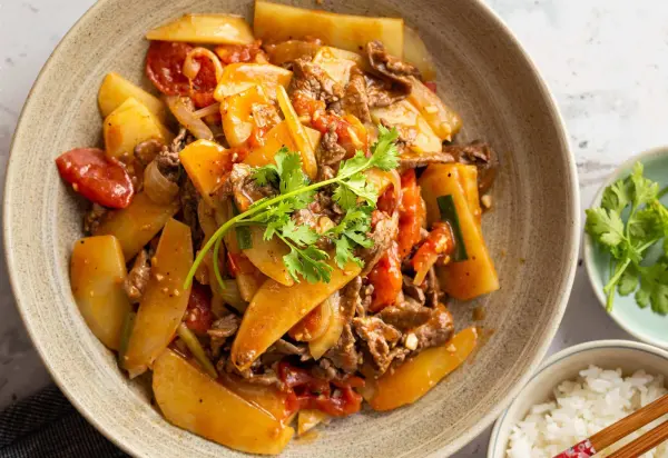 Đĩa thức ăn với thịt bò xào, cà chua, và khoai tây, được trang trí bằng rau mùi.